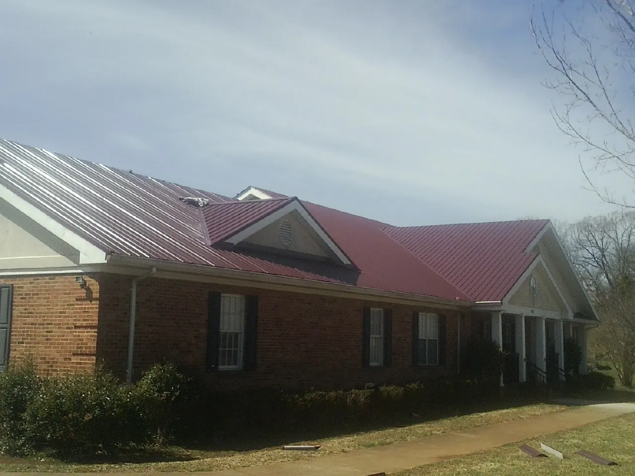 Red metal roof with gabled entries on a long brick building, from a Hail Damage Roof Repair job in Springdale