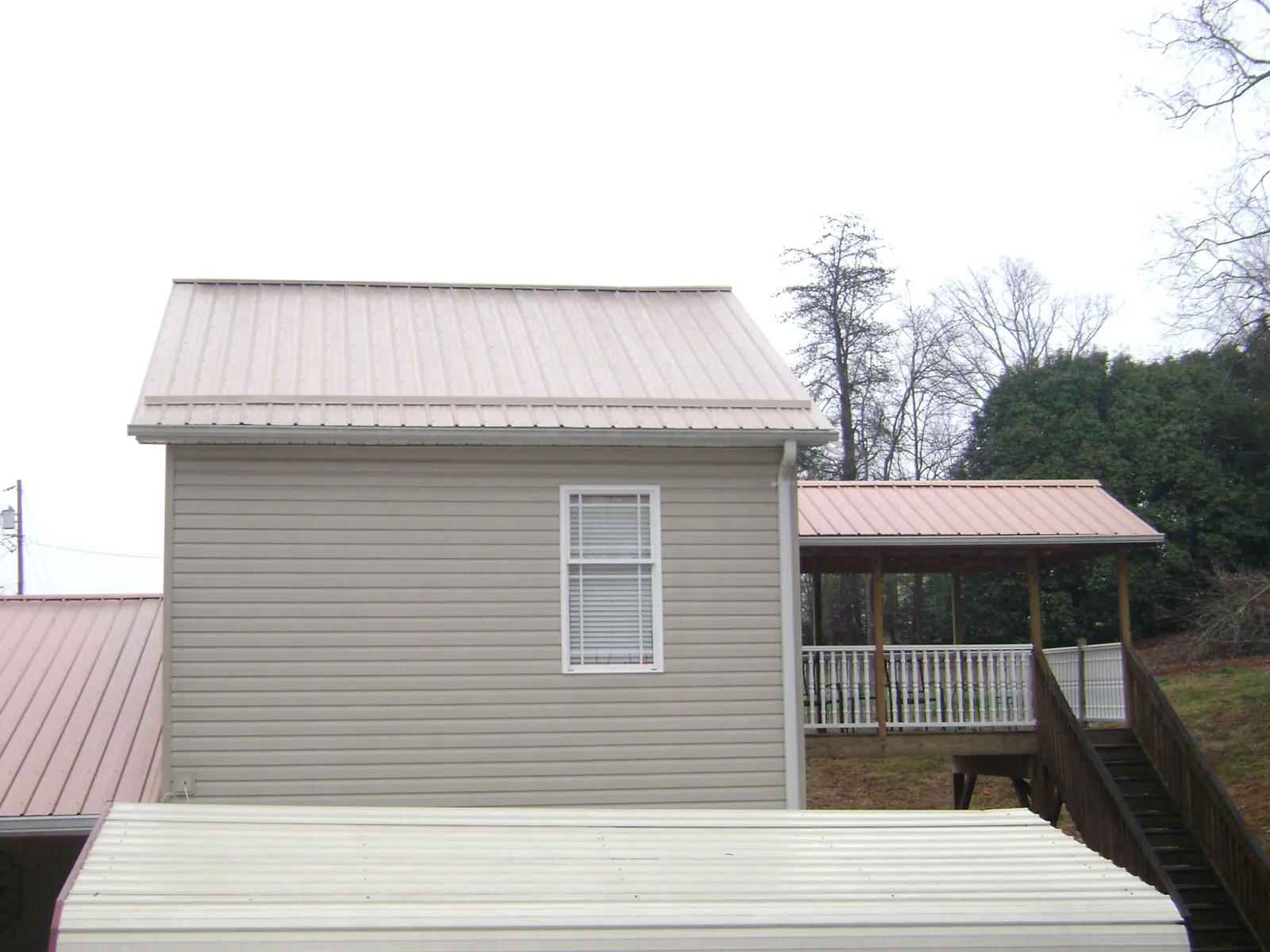 Tan metal roofs on a two story addition and attached porch, from a Roof Replacement job in Springdale